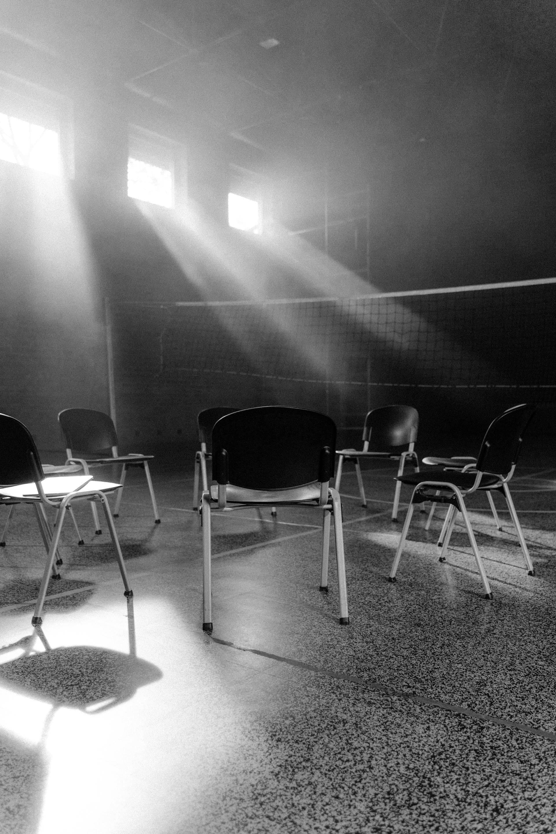 Empty chairs arranged in a circle in a quiet hall, daylight falling through high windows.